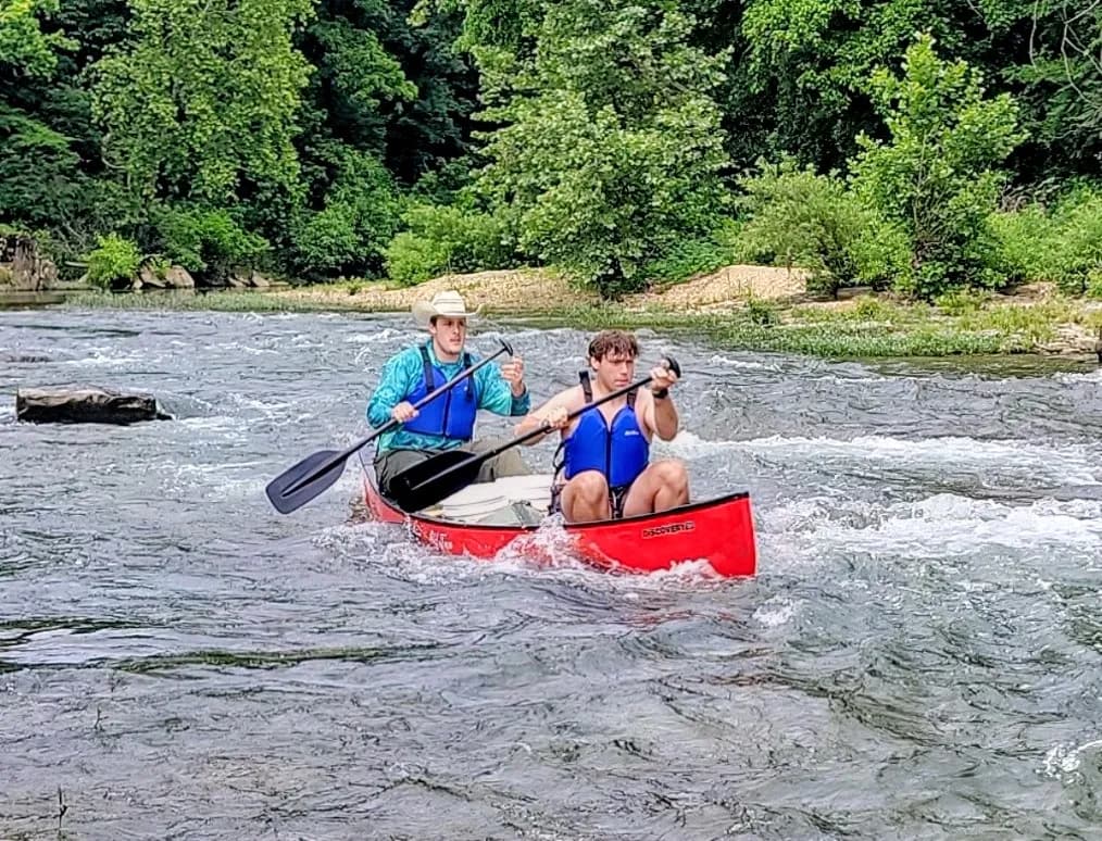 Two young men paddling a canoe through a river rapid