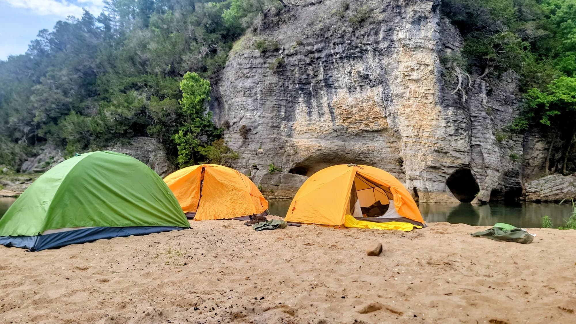 Tents pitched on a sandbar beneath a canyon wall at base camp